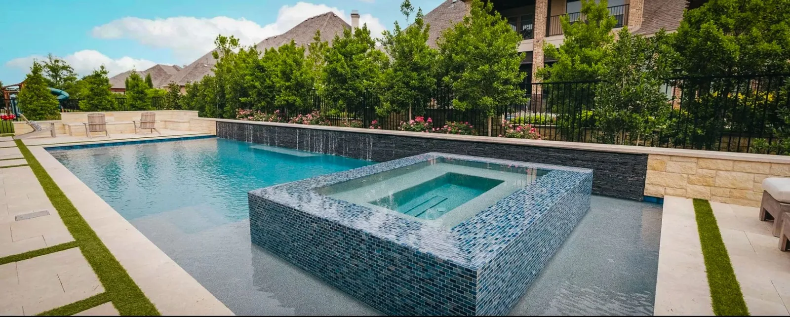 Rectangular pool with a raised glass tile spa and a stone deck