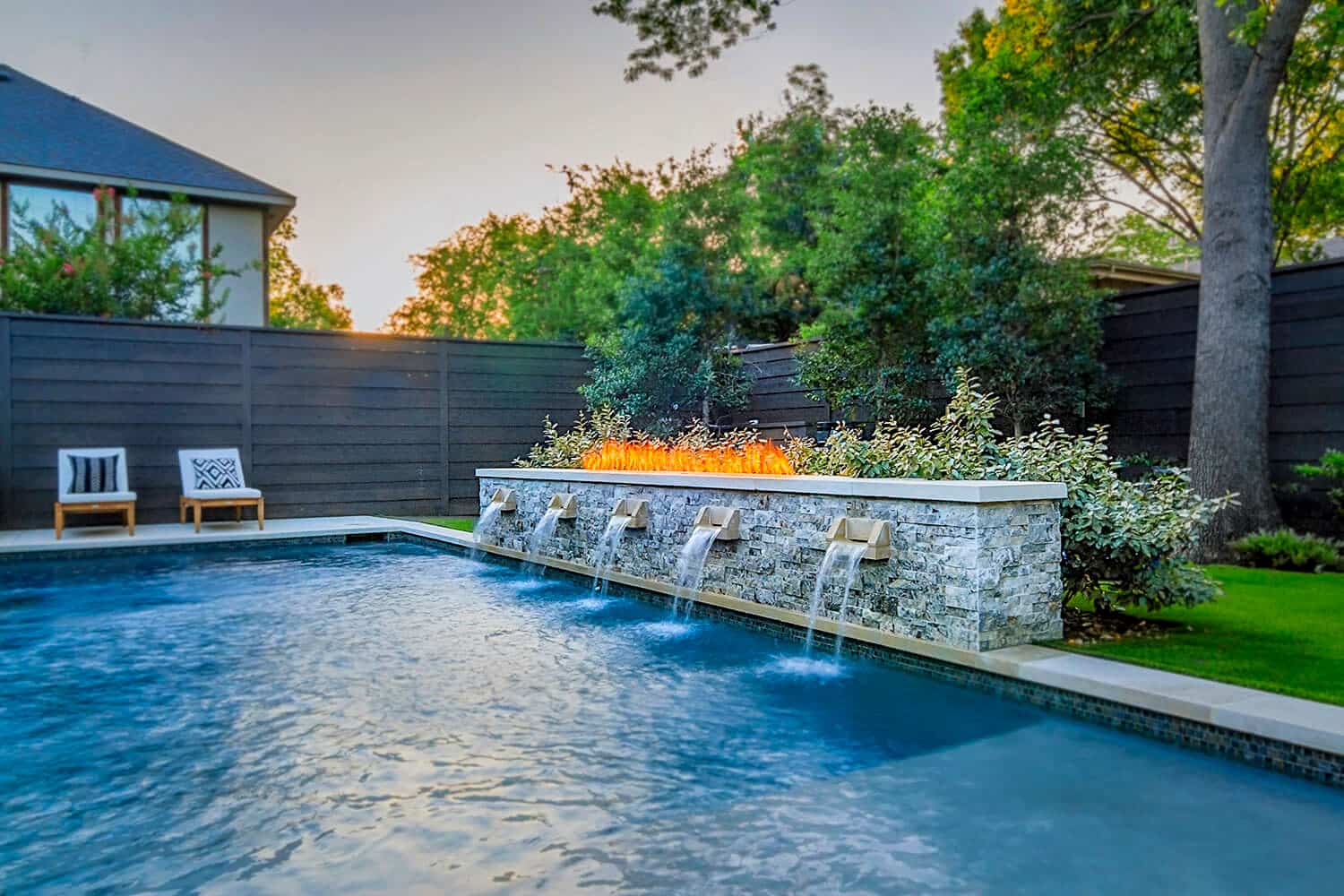 Pool with sheer descent waterfalls below a stone fire feature